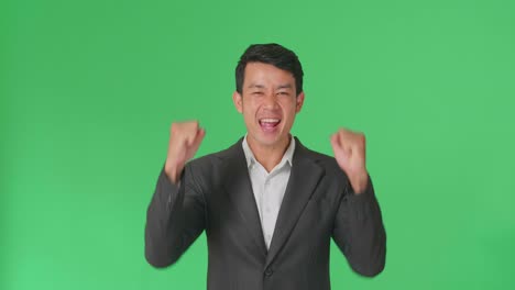 cheerful young asian business man celebrating while standing on green screen in the studio