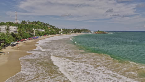 Mirissa-Sri-Lanka-Aerial-v4-fly-along-exotic-sandy-beach-towards-Parrot-rock-capturing-summer-seascape-of-swelling-surf-and-rip-currents-waves-crashing-the-shore---Shot-with-Mavic-3-Cine---April-2023