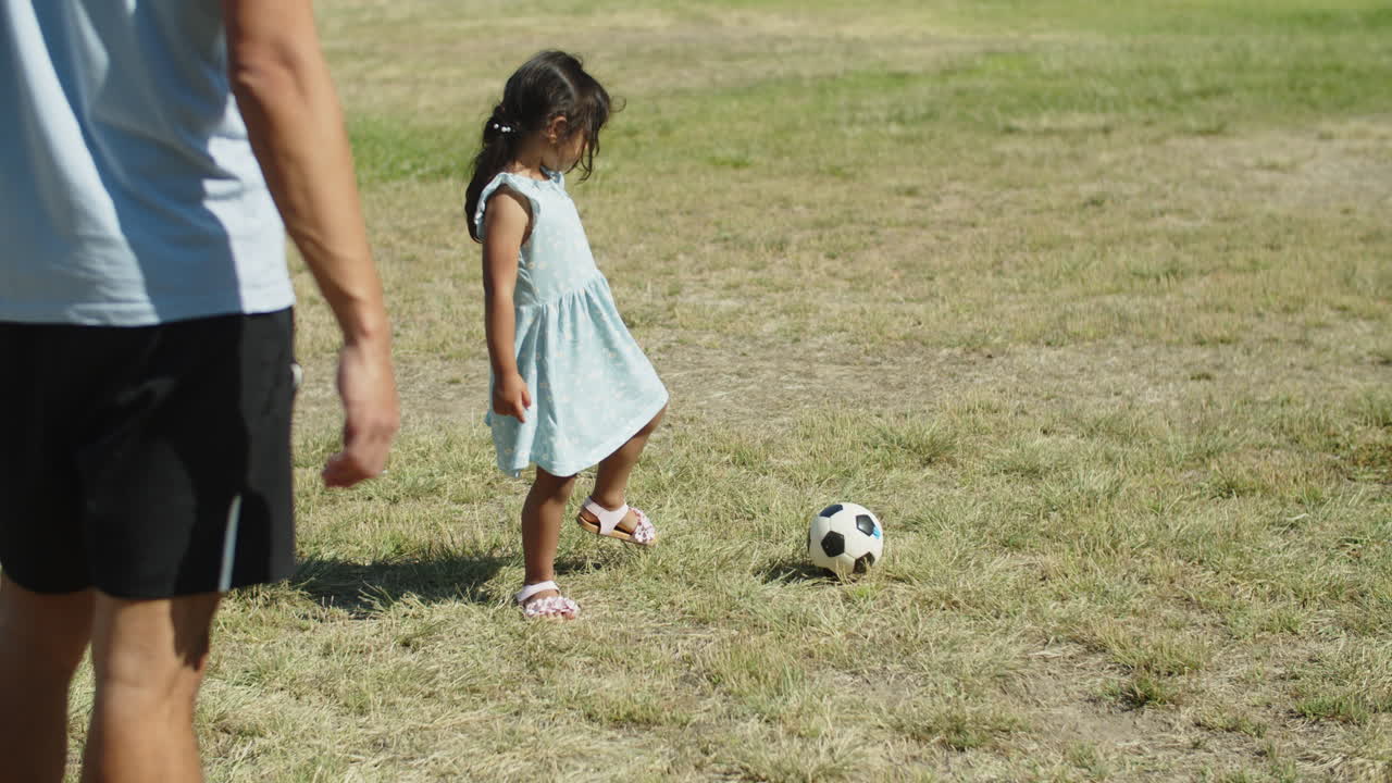 Menina asiática fofa brincando de bola com o pai no parque.