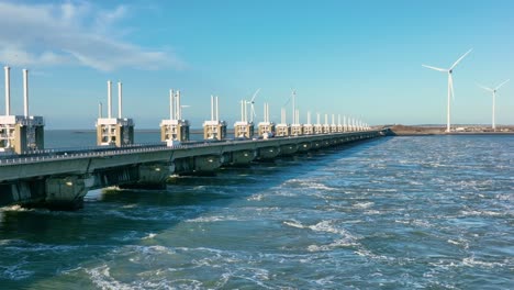 Toma-Aérea-Del-Tráfico-En-La-Barrera-Contra-La-Marejada-Ciclónica-Del-Este-De-Scheldt-Y-Turbinas-Eólicas-En-Zelanda,-Los-Países-Bajos,-En-Un-Hermoso-Día-Soleado