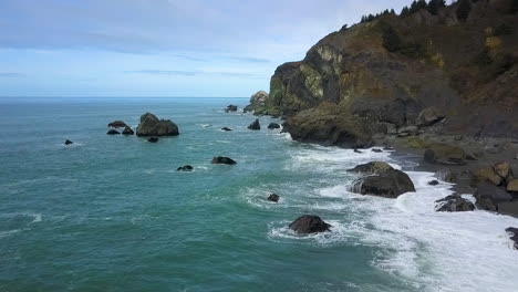 stationary aerial drone of pacific northwest rocky coastline, cliffs, and beach on overcast day