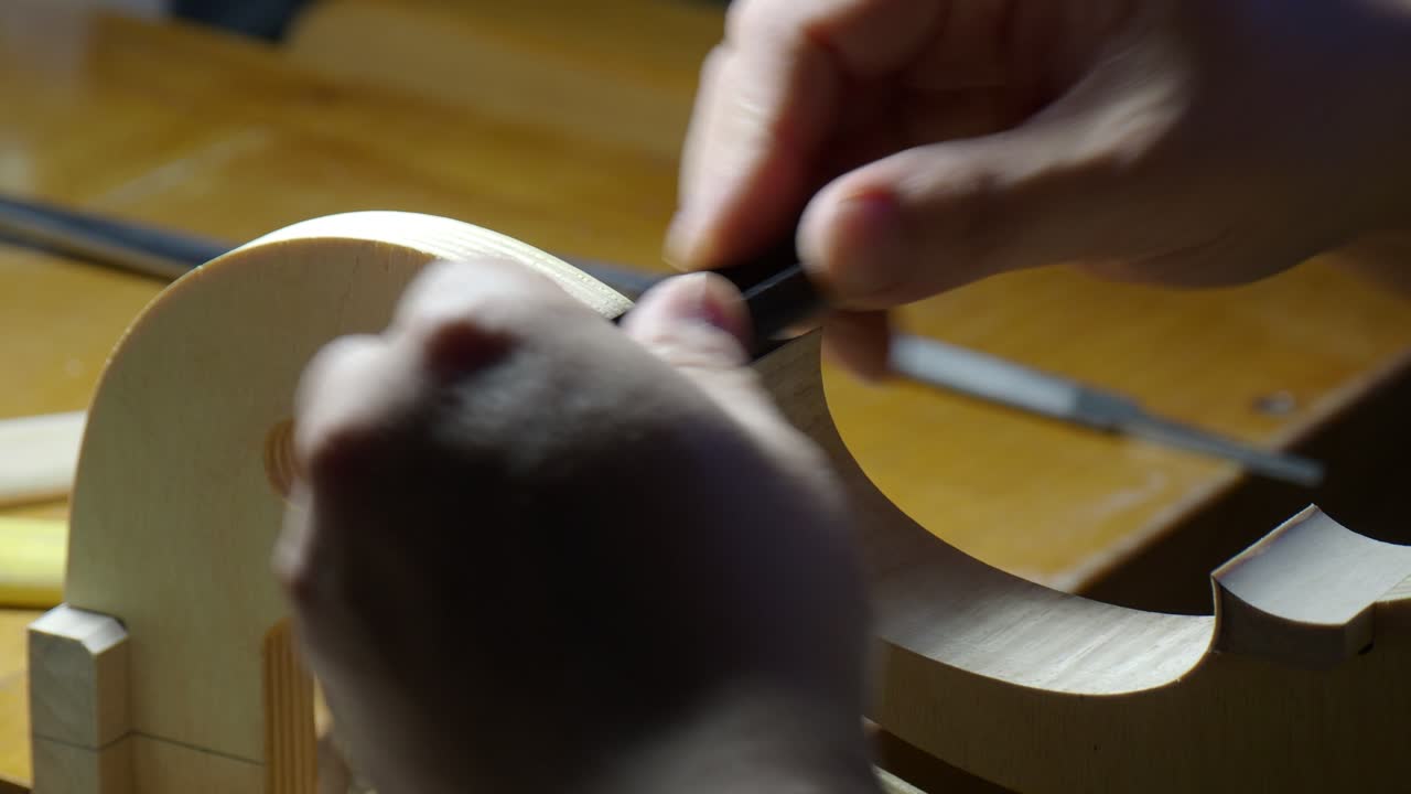 Violin rib and edge being shaped and refined on internal mold by luthier using small finger plane to achieve precise thickness and smooth curve during instrument construction in traditional workshop,