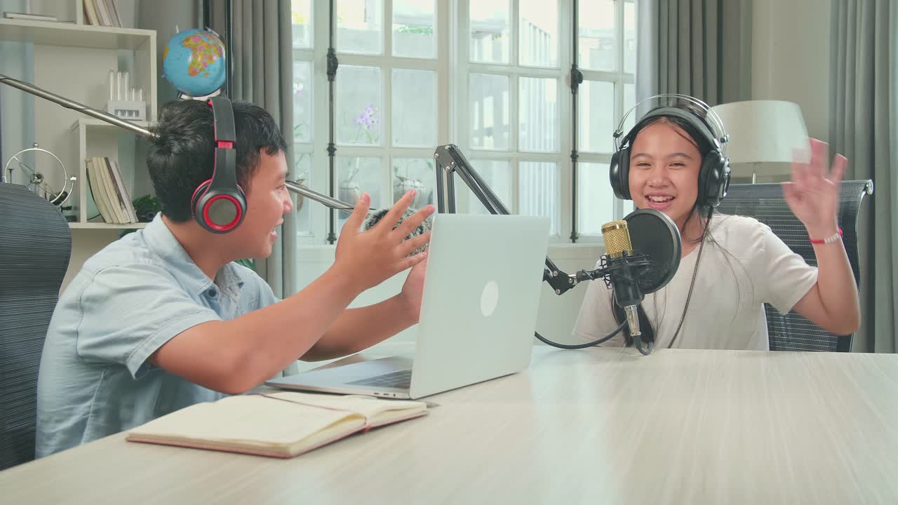 Asian Boy Host Record Podcast Use Microphone Wear Headphone With Laptop Interview Guest Conversation In His Home Studio, They'Re Talking And Looking At Camera For Content. Content Creator Concept
