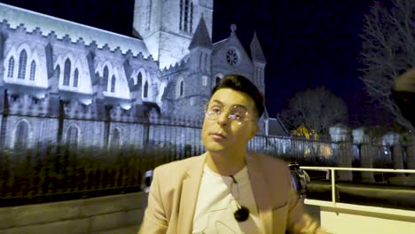 irish television star comedian alan mcgarry extoling the virtues of dublin city on a horse drawn carriage tour with the ancient flood lit christchurch cathedral in the background