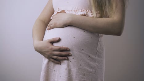 pregnant woman strokes tummy in white background closeup