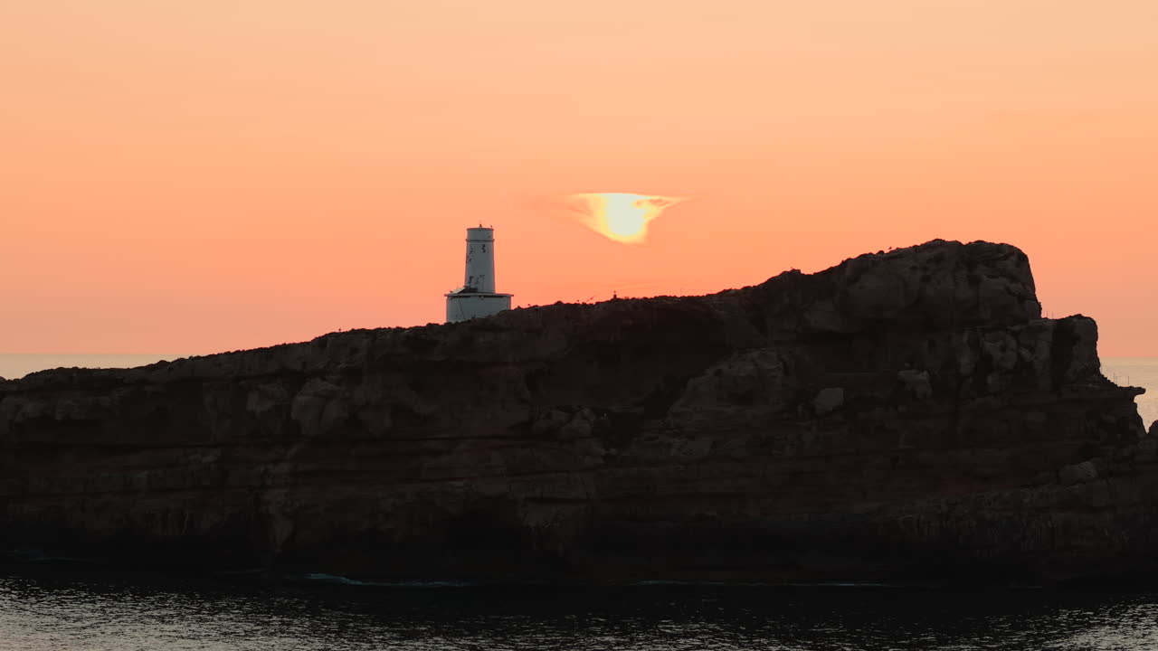 Faro su un'isola rocciosa al tramonto