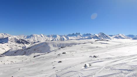 toma aérea de un área de deportes de invierno con pistas de esquiadores fuera de pista en primer plano y esquiadores en una pendiente preparada en el fondo