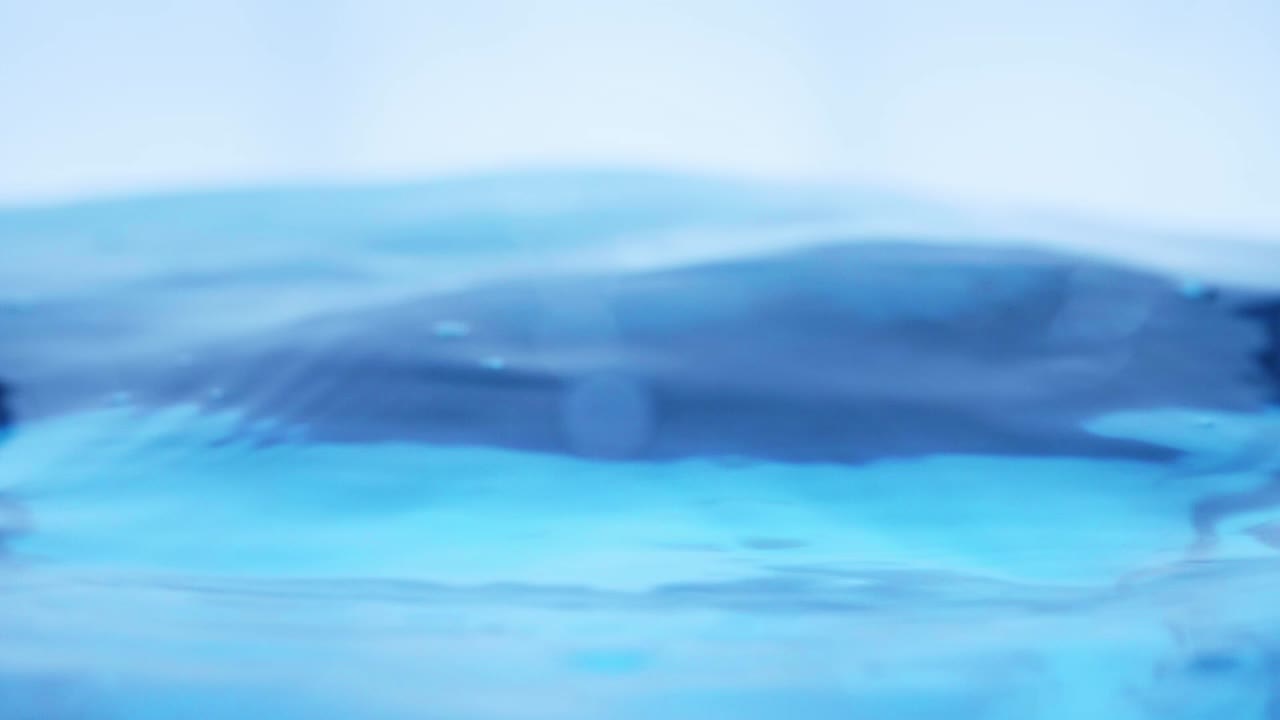 슬로우 모션의 깨끗한 물 표면은 물이 튀는 상점으로 화면을 채우고 기포로 액체 표면을 흔들고 있습니다.