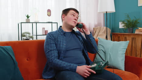 Man-making-old-fashioned-retro-telephone-conversation-talking-with-friends-sitting-on-home-sofa