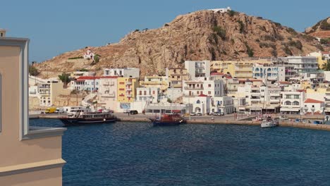 Cinematic drone flight near the Eparchy building in Karpathos, unveiling the vibrant seafront, harbor, and stunning coastal views under bright, clear skies