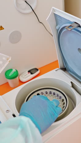 modern apparatus for checking samples in lab. hand in blue glove puts plastic tubes with blood tests to orifices of centrifuge. vertical video