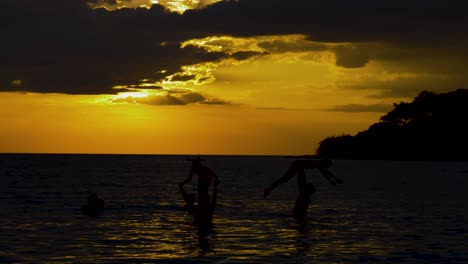 Silhouetten-Der-Familie,-Die-Im-Meer-Spielt,-Mit-Der-Untergehenden-Sonne-Im-Hintergrund