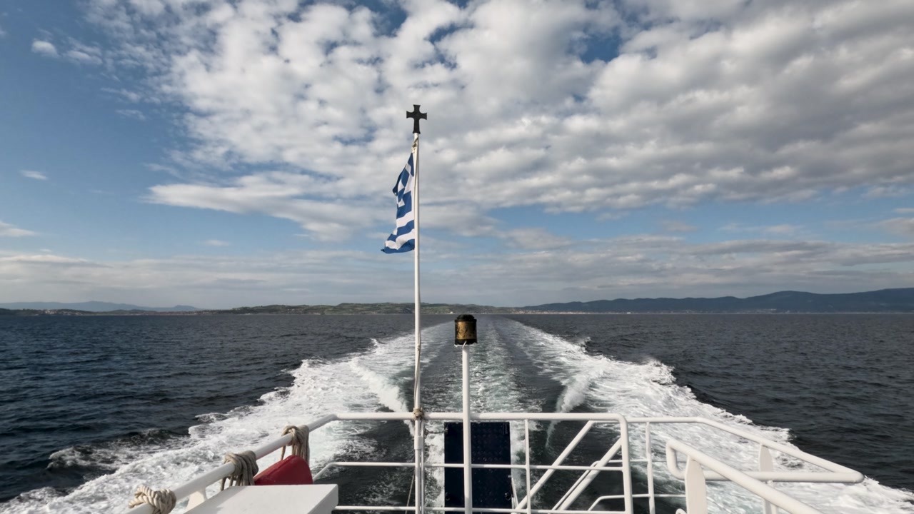 A group travels to a quiet island surrounded by water. The sun shines brightly as they get closer to the shore. Waves gently lap against the rocky coast.