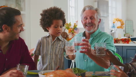 Familia-Multigeneracional-Celebrando-El-Día-De-Acción-De-Gracias-En-Casa-Comiendo-Y-Animando-Con-Agua