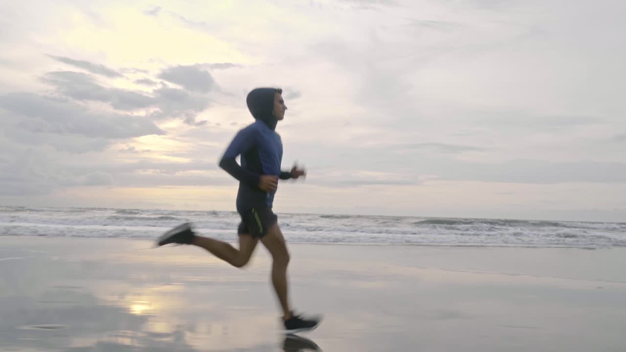 vídeo cinematográfico de un hombre en forma y saludable corriendo rápido por la playa húmeda y fría de cornualles en inglaterra justo antes de que el sol haya salido por completo por la mañana