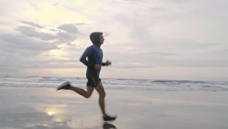 cinematic low down video of a fit and healthy man running fast down the wet and cold beach in cornwall in england just before the sun has fully risen in the morning