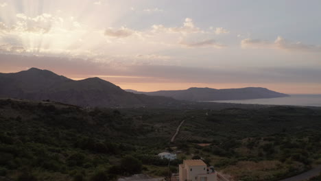 aerial pull away of landscape and mountains in crete, greece at sunset with sun flares and warm colours