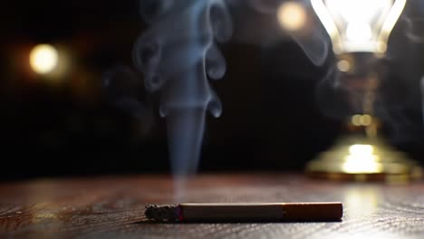 a tranquil evening: a smoking cigarette sends up wisps of smoke under the gentle glow of a lantern's light, creating a serene and reflective atmosphere