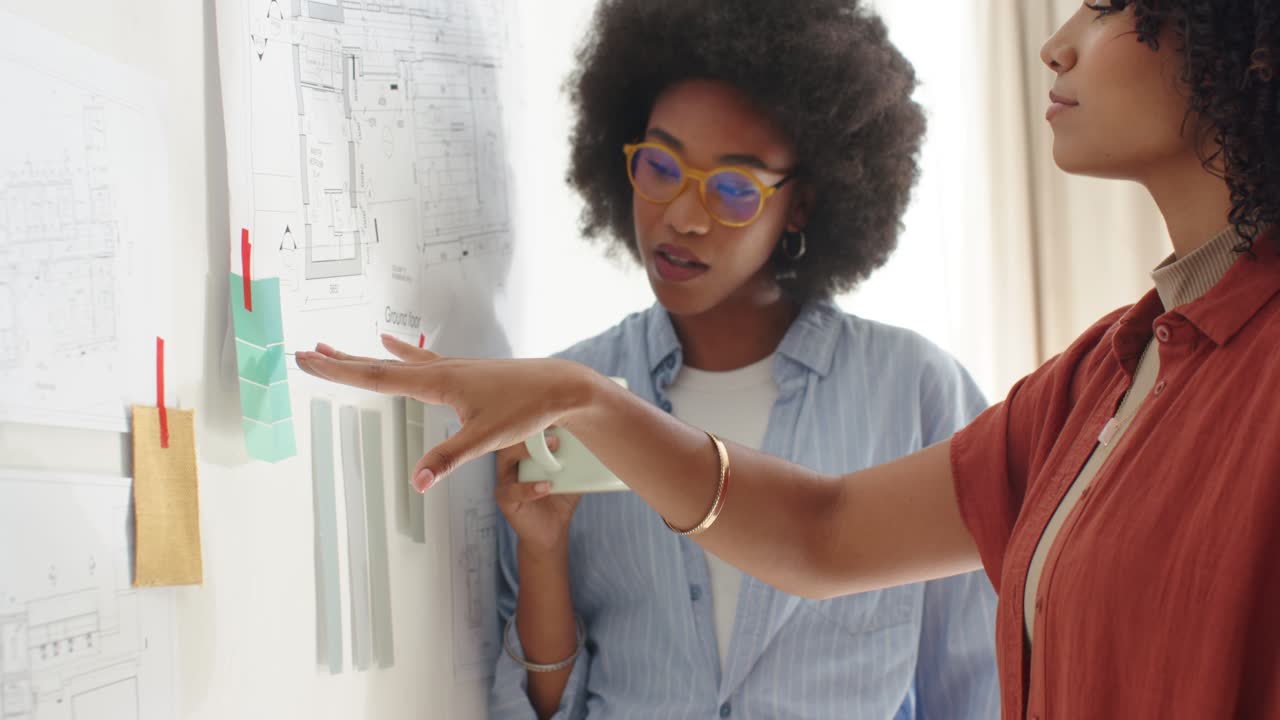 Diverse female coworkers reviewing plan in studio, right woman pointing swatches, spurring decision