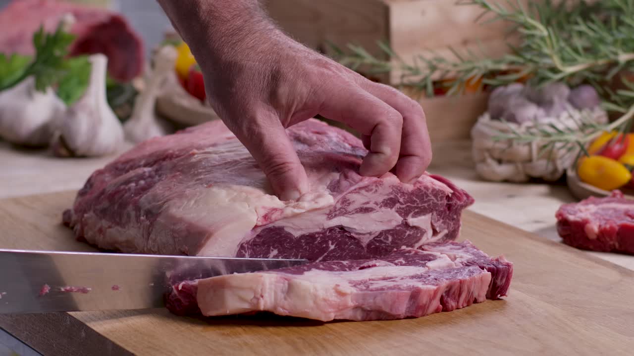 Close up of a butcher's hands expertly carving a premium marbled ribeye steak from a large raw beef roast on a wooden board for a meat lover's feast