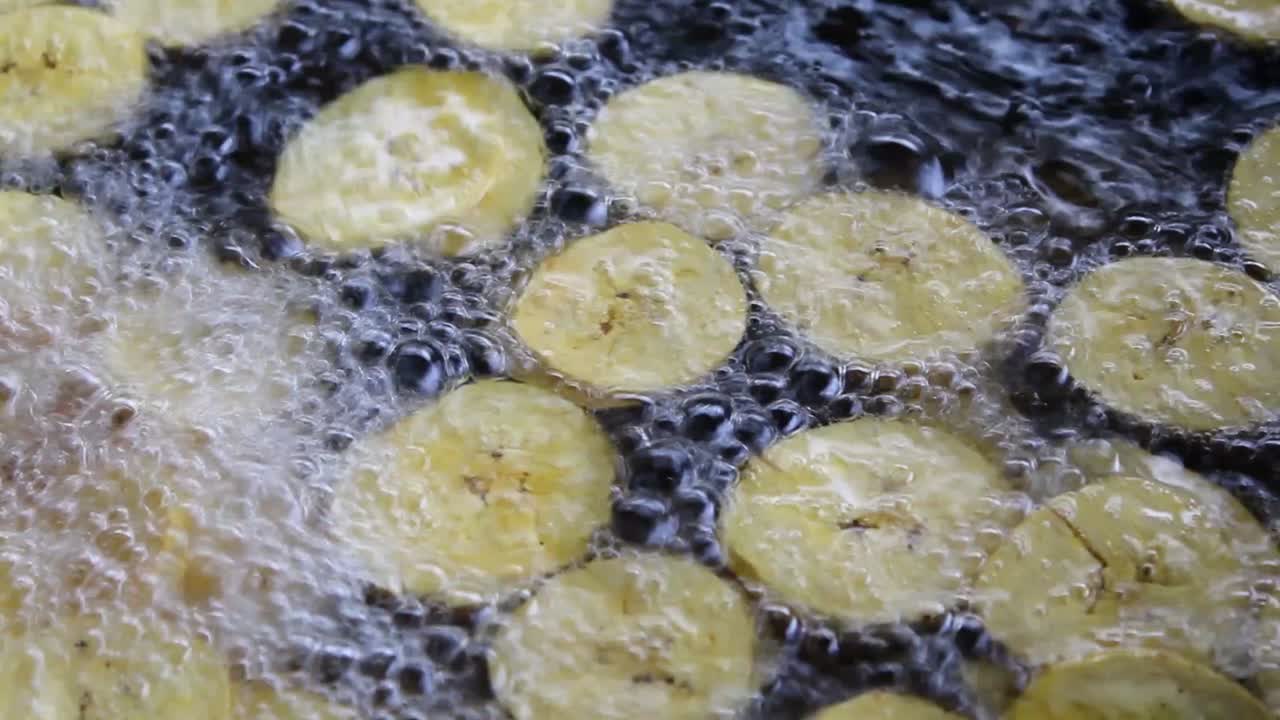 plátanos fritos para cocinar, plátanos fritos flotando en aceite hirviendo, primer plano de plátanos fritos, chips de plátano en aceite hirviendo