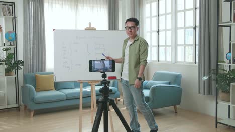 asian male teacher with glasses shoots video by smartphone camera while teaching english at home