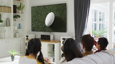 asian family watching tv with rugby ball at stadium on screen