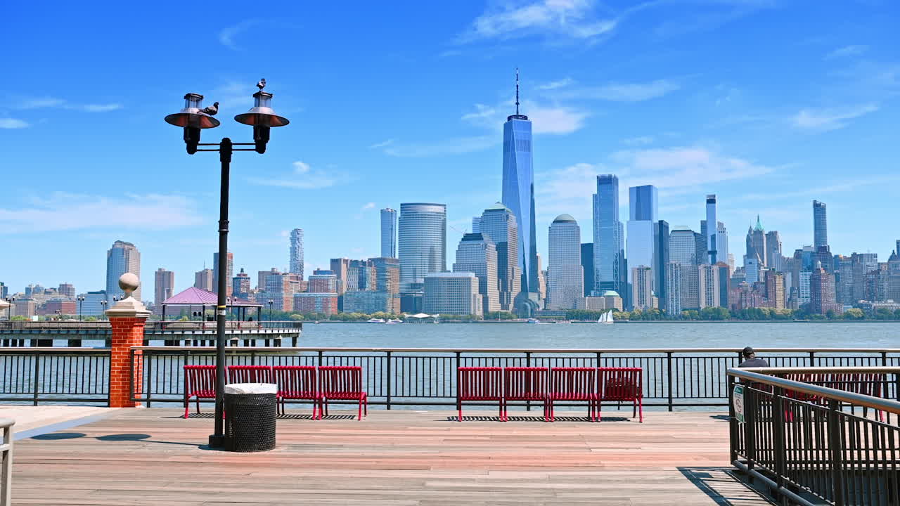 A walk by the beautiful pier with lanterns and red benches in sunny Jersey. Spectacular scenery of Manhattan over the Hudson