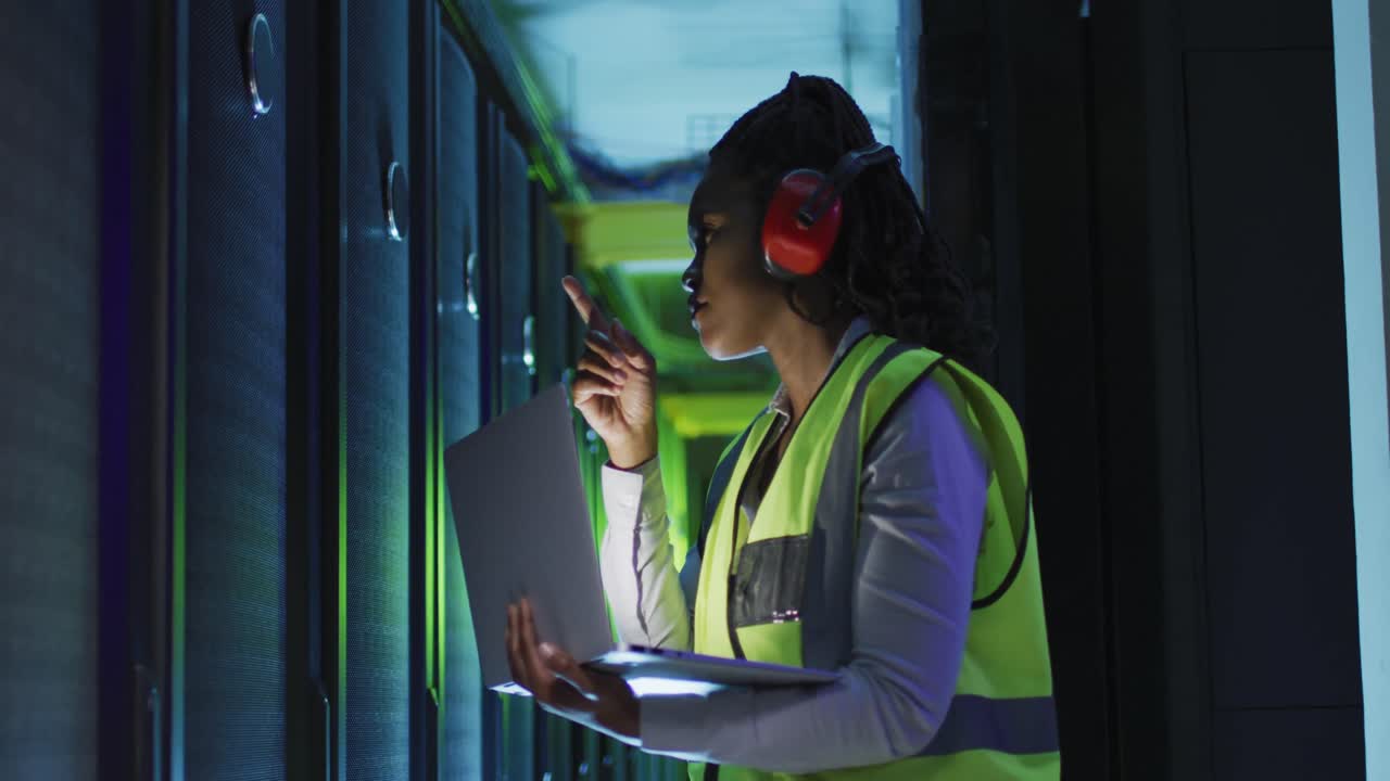 African american female computer technician using laptop working in business server room