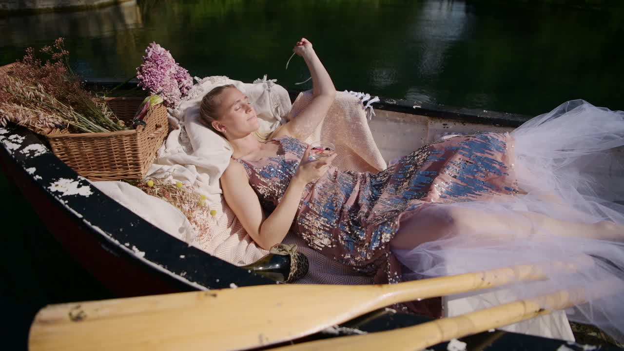 Woman daydreaming on sunny day laying down in a traditional rowboat, static shot