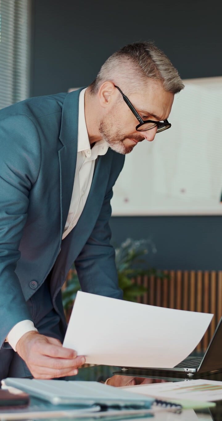 Mature Businessman Reviewing Documents and Working on Laptop in Office