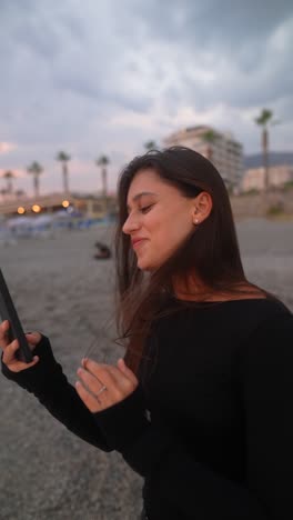 mujer usando el teléfono en una playa al atardecer