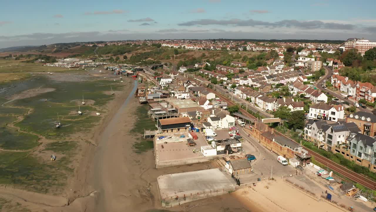 volando hacia atrás y girando para revelar una playa de arena y casas sobre un pueblo pesquero costero sobre pantanos