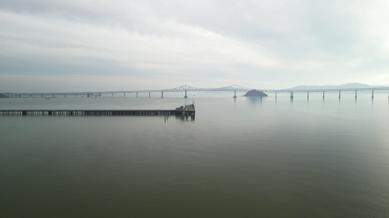 Drone aligns wooden pier with Richmond Bridge from Point Molate Beach Richmond California USA