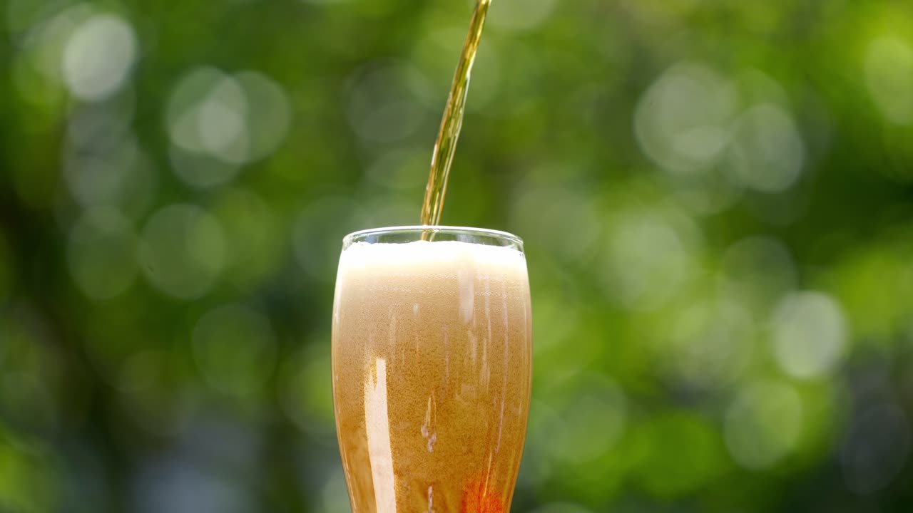 Pouring fresh beer with foam running down. Stream of beer pours into a beer glass against blur green background. Close-up.