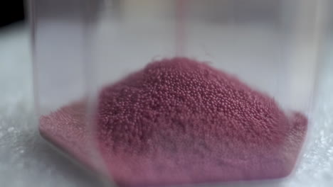 macro shot of pink sand particles in hourglass sand timer clock