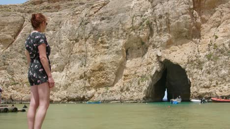 chica de pie en la orilla mirando la cueva del mar con barcos en un día soleado en el mar interior, malta