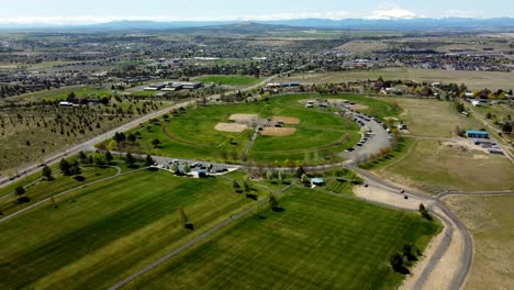 us, oregon, madras, juniper hill park, 2025-04-19 - drone view flying over the juniper hill sports complex. with baseball fields, soccer fields, parking, and a view of the city beyond.