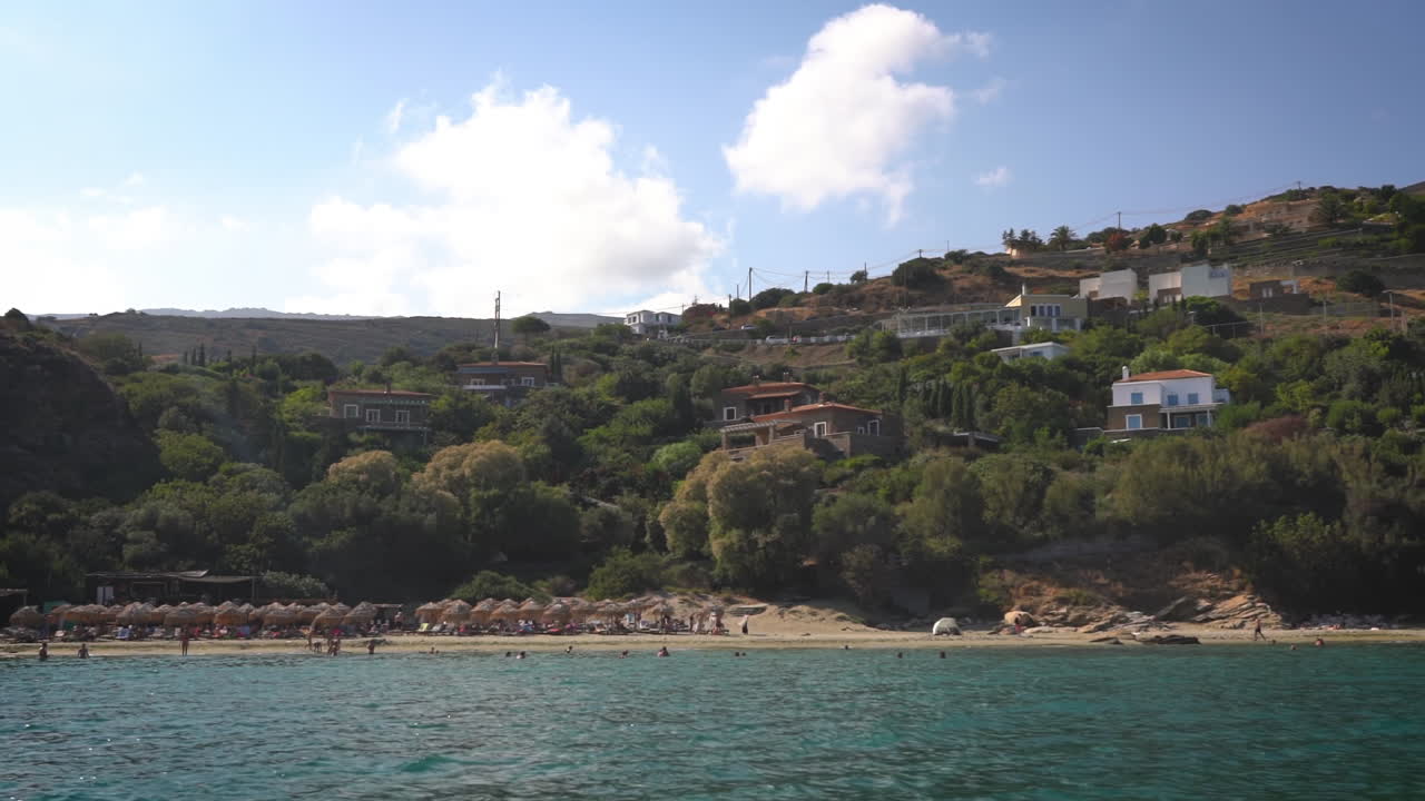 A serene beach scene with people relaxing and swimming, set against green hills and a clear sky