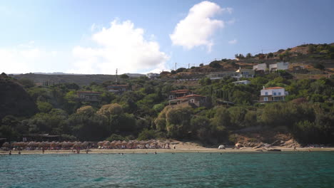 A-serene-beach-scene-with-people-relaxing-and-swimming,-set-against-green-hills-and-a-clear-sky