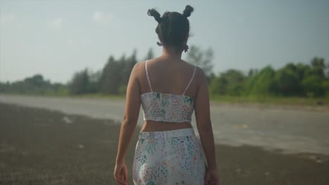 A-young-girl-dressed-in-a-light-top-and-shorts-walks-along-an-empty-beach-in-Goa,-near-the-Arabian-Sea