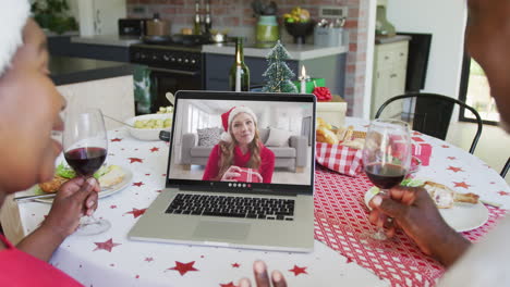 una pareja afroamericana con vino usando una computadora portátil para una videollamada de navidad con una mujer feliz en la pantalla