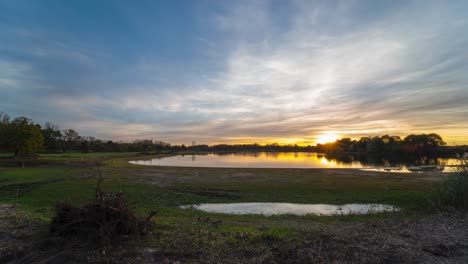 La-Majestuosa-Puesta-De-Sol-Se-Refleja-En-El-Agua-Del-Lago-En-Un-Paisaje-Rural-Vibrante,-Lente-Gran-Angular