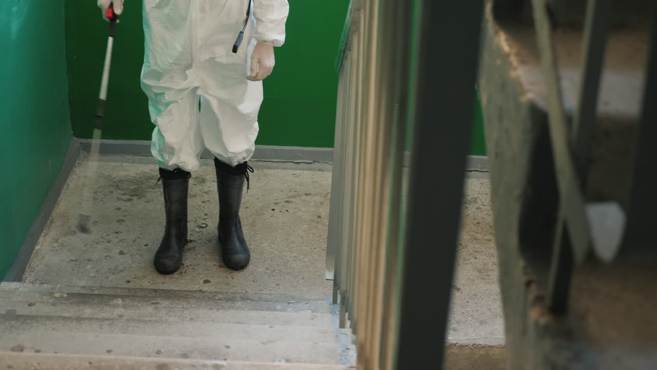 un hombre con uniforme protector rociando los escalones de la casa con un antiséptico