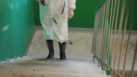un hombre con uniforme protector rociando los escalones de la casa con un antiséptico