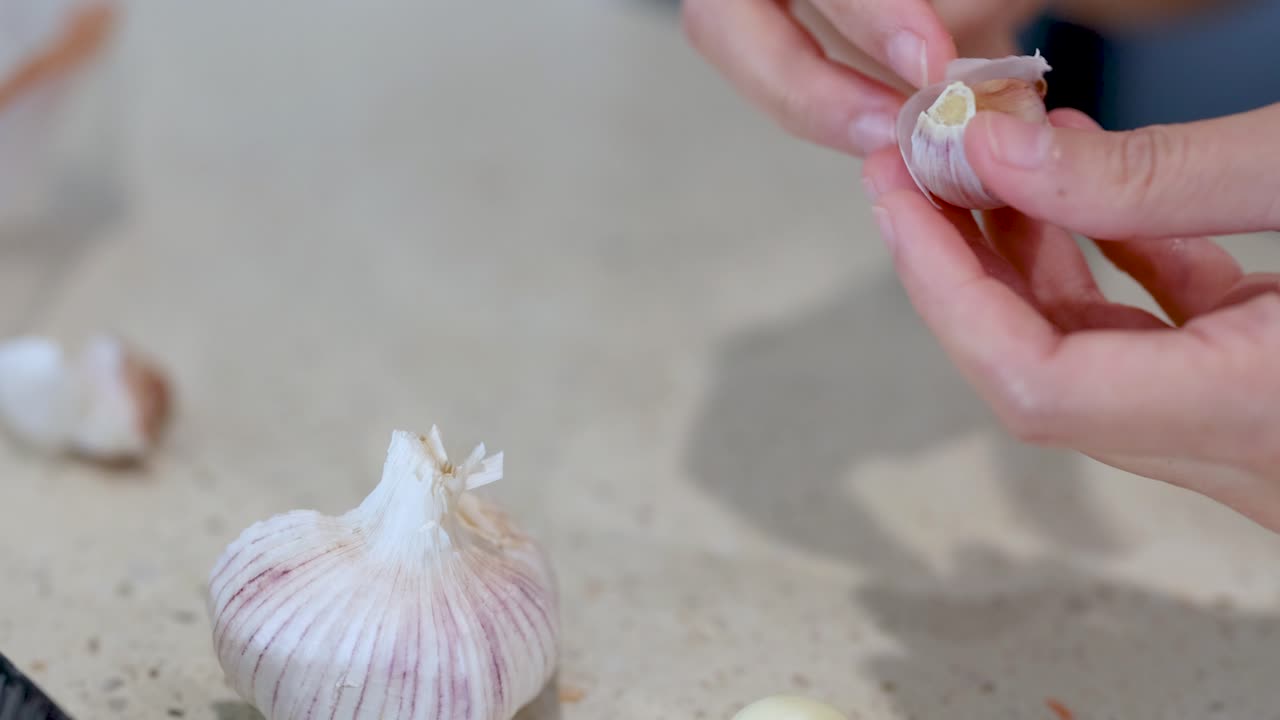 Close-up of hands peeling garlic cloves on a kitchen counter with soft lighting and a neutral background