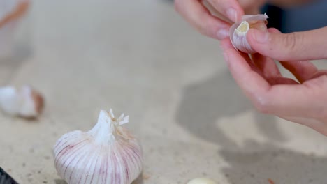 close-up of hands peeling garlic cloves on a kitchen counter with soft lighting and a neutral background