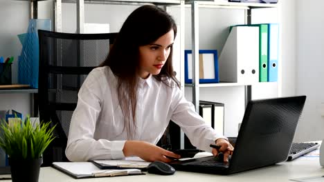 mujer de negocios trabajando en una computadora portátil y contando con una calculadora en una oficina moderna
