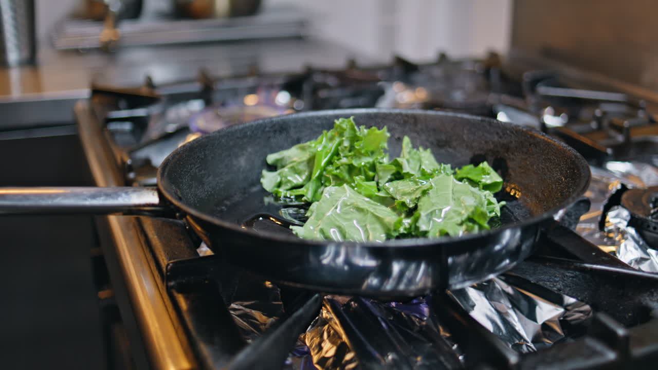 Man frying fresh greens in pan at restaurant kitchen closeup. Unknown worker