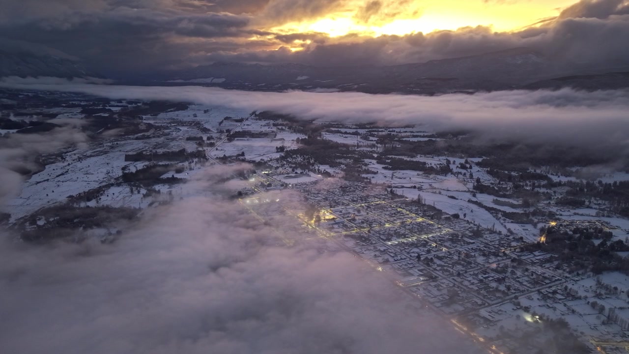 Aerial orbit of Melipeuco, in Chile, covered in snow and shrouded in a thin cloud, with an epic sunset as a backdrop; a wild, natural setting in the Andean Araucanía region.